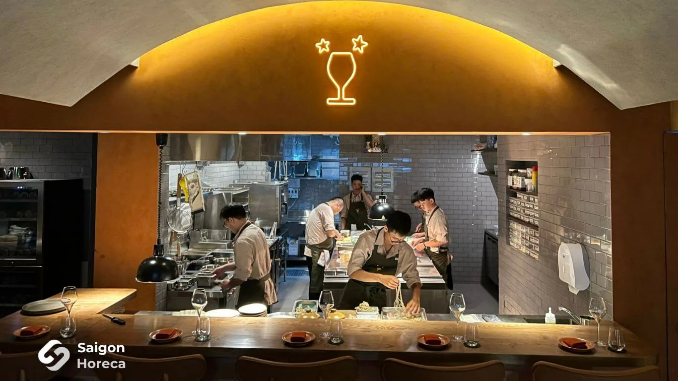 Oak bar and arched open kitchen pass bathed in wine-glass neon glow at Little Bear Thao Dien