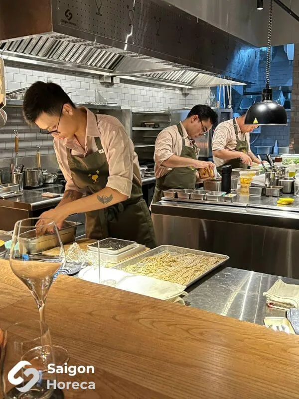 Photograph of chefs executing meticulous plating along the hot cooking line at Little Bear Thao Dien