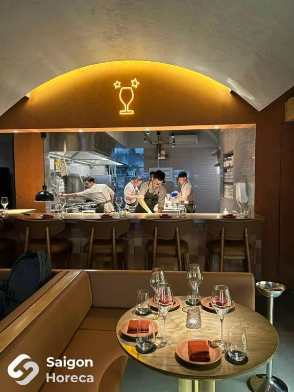 Round dining table overlooking the arched open kitchen with neon wine glass sign at Little Bear Thao Dien
