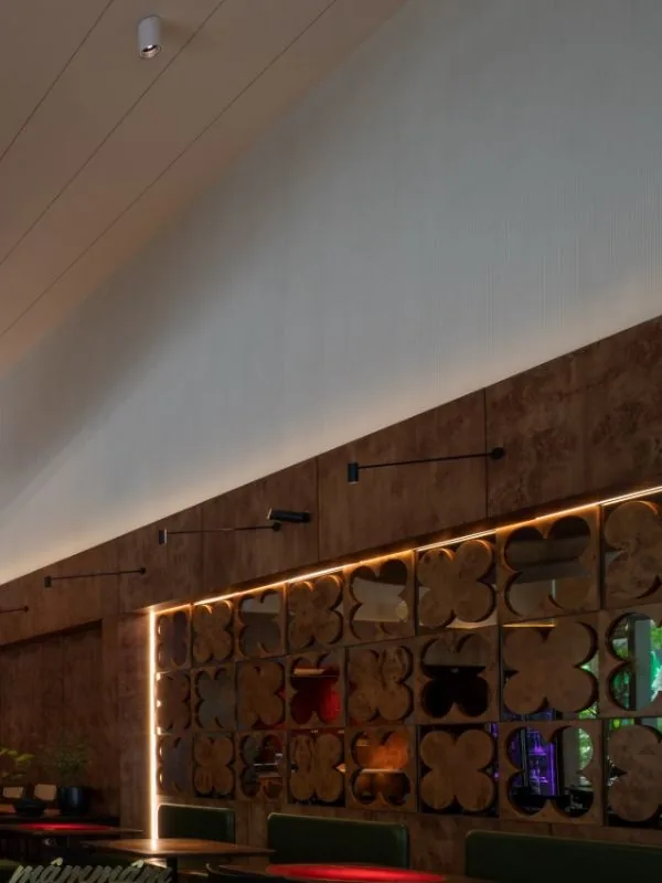Vách ngăn trang trí họa tiết hoa bốn cánh ốp đá hắt sáng LED ấm trong phòng ăn Mâm Mâm, kết hợp trần dốc trắng và khu ghế bọc xanh
