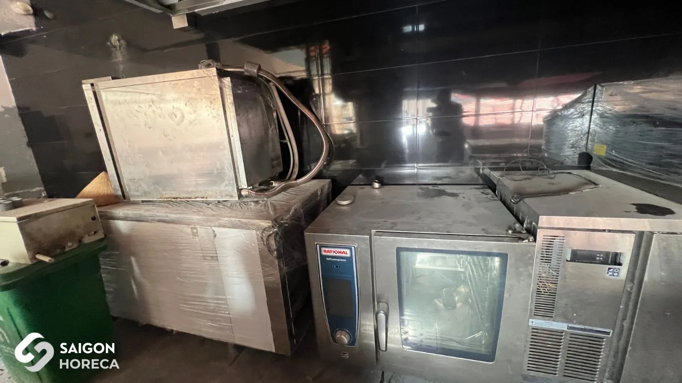 Giai đoạn lắp đặt thiết bị bếp tại Sol Kitchen & Bar Quận 7: lò combi RATIONAL, tủ inox và tủ mát còn bọc nilon đặt sát tường ốp gạch đen của công trường
