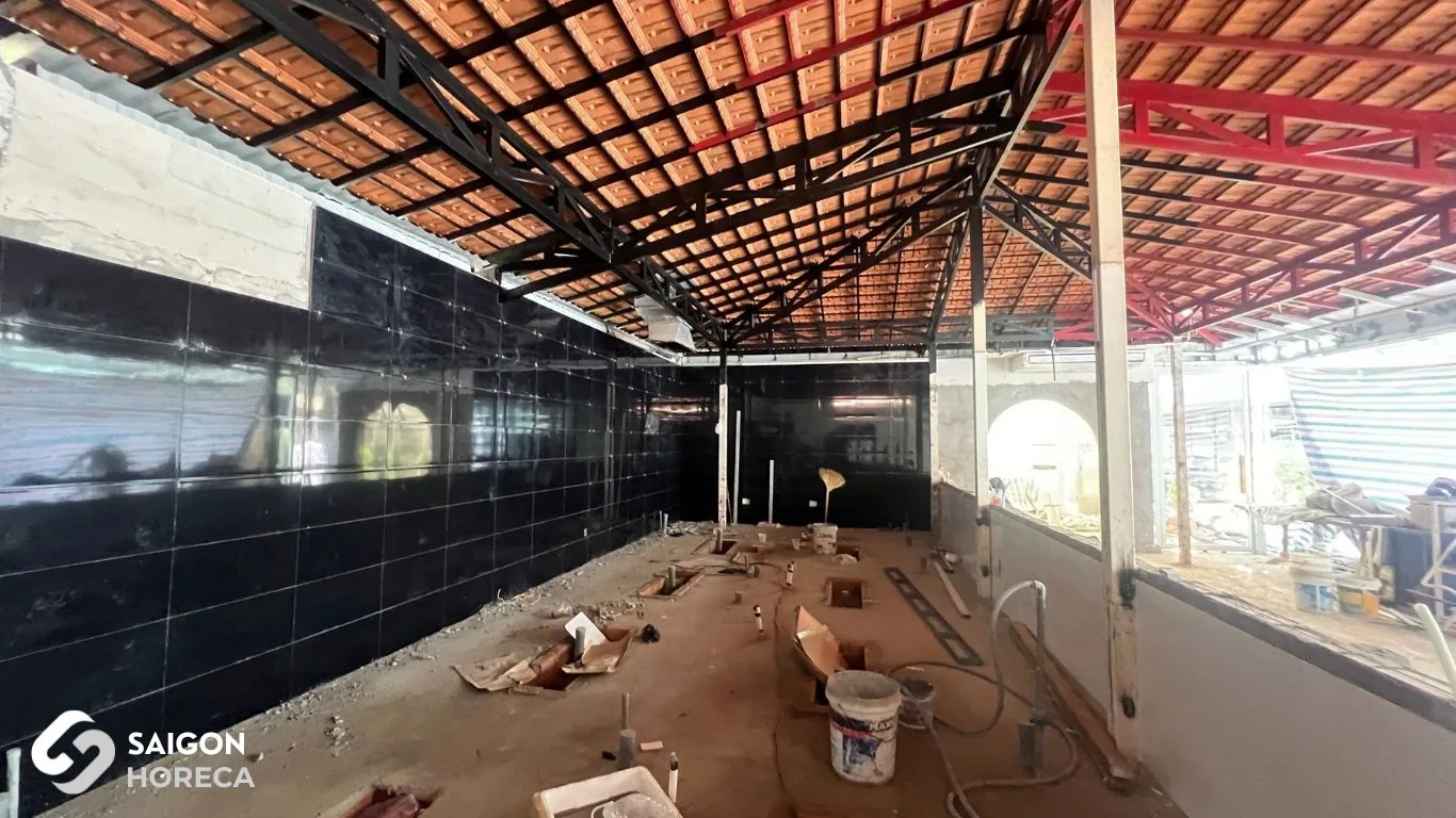 Công trường đang thi công cải tạo dưới mái lợp ngói, tường ốp gạch đen, sàn bê tông ngổn ngang vật liệu xây dựng tại Sol Kitchen & Bar Quận 7