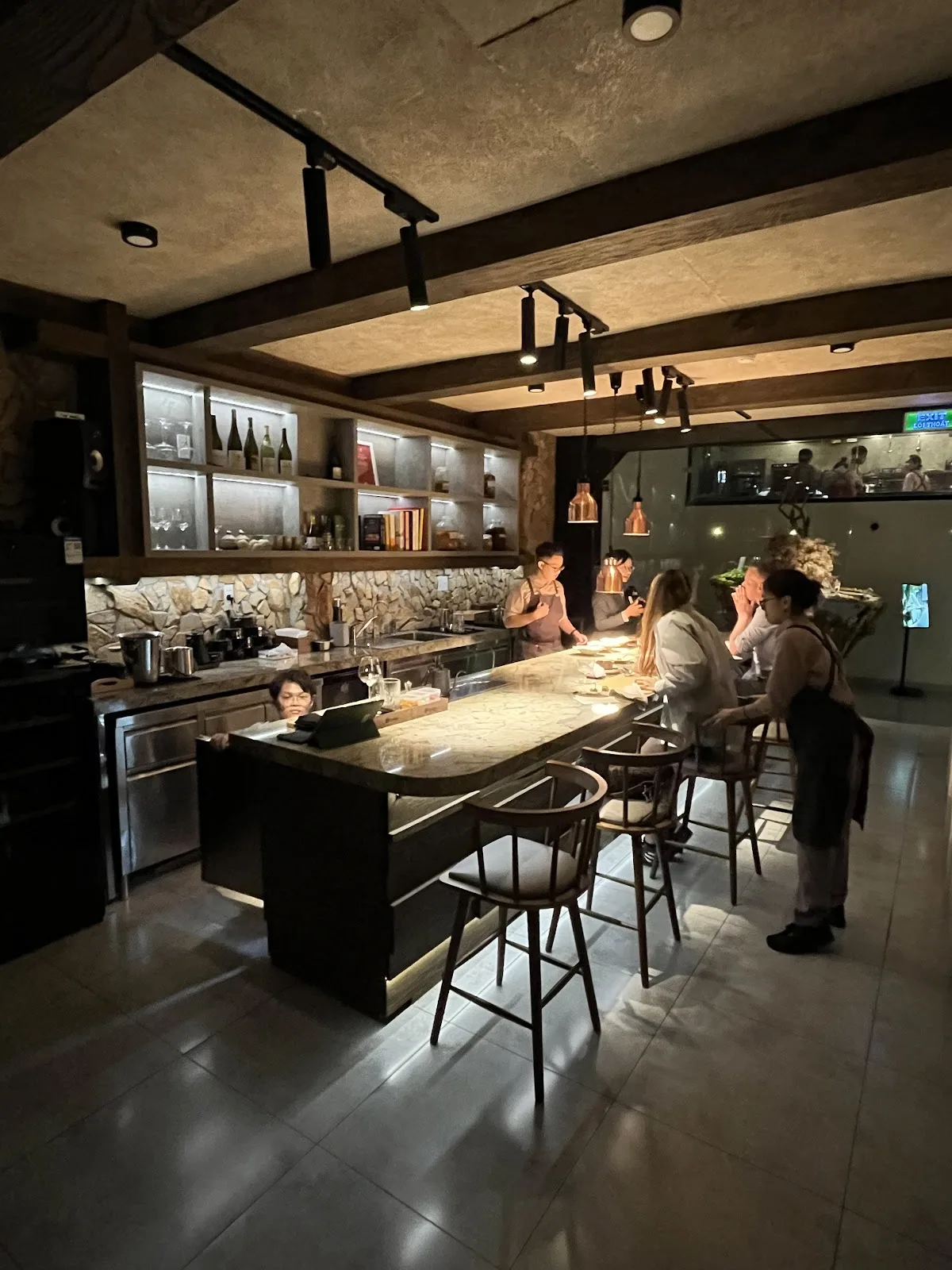 Quầy bar mặt đá cẩm thạch có khách ngồi, phía sau là bếp mở