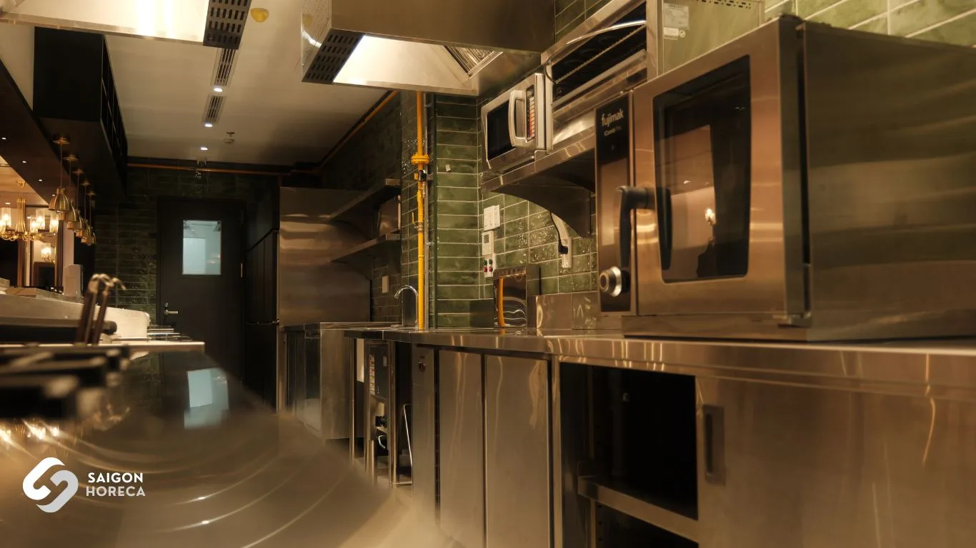 Stainless steel prep counters and sinks beneath vintage brass pendant lamps at The Royal commercial kitchen