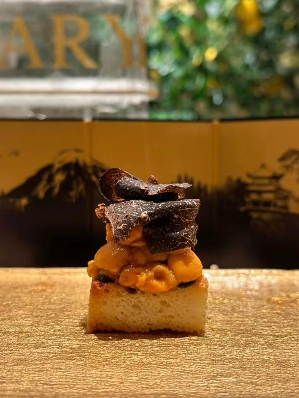 Bánh nướng phủ cồi nhím biển uni và lát nấm truffle đen trước bình phong vàng vẽ núi Phú Sĩ