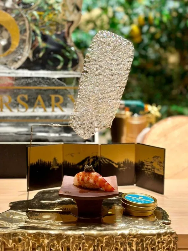 Nigiri sushi tôm ngọt Amaebi phủ nhũ vàng và Caviar đặt trước bình phong vẽ phong cảnh Nhật Bản cổ kính